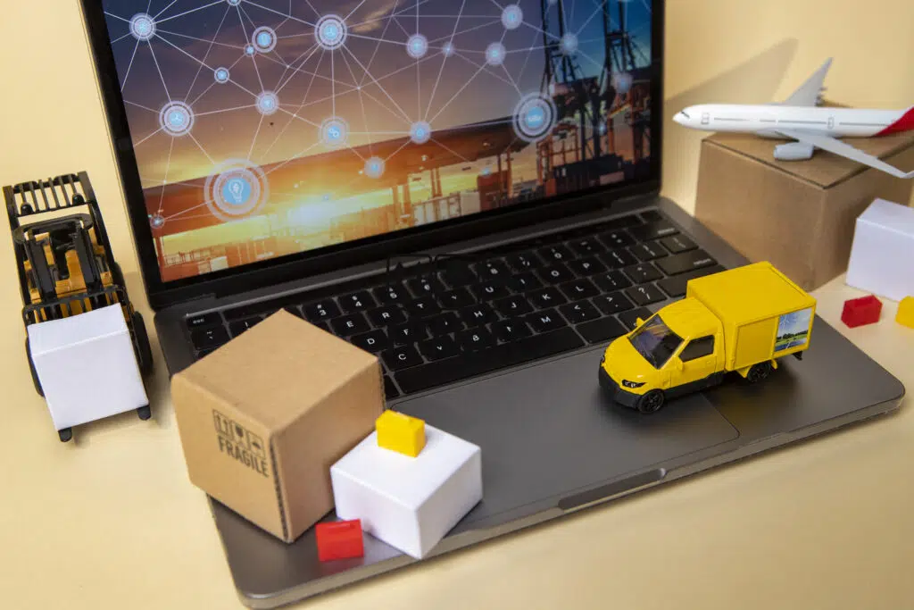 Miniatura de caminhão e caixas sobre um notebook representando a logística integrada.
